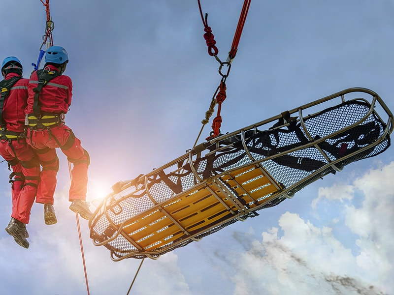 Rescue team performs an aerial lift operation with a basket stretcher, ready for mountain or high-angle emergencies.