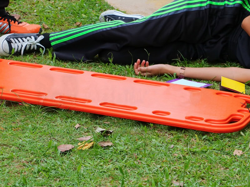Injured person lies beside a bright orange spine board on grass