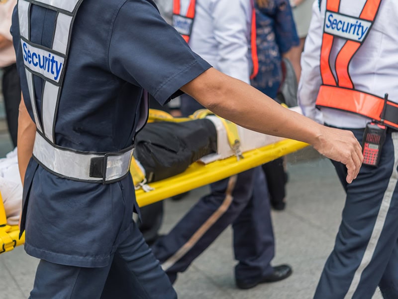 Security personnel carry an injured individual on a stretcher through a crowded area during an emergency.