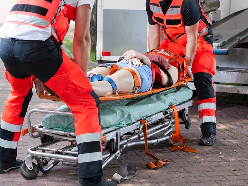 Paramedics carefully lift a secured patient on a spine board onto a stretcher for ambulance transport.