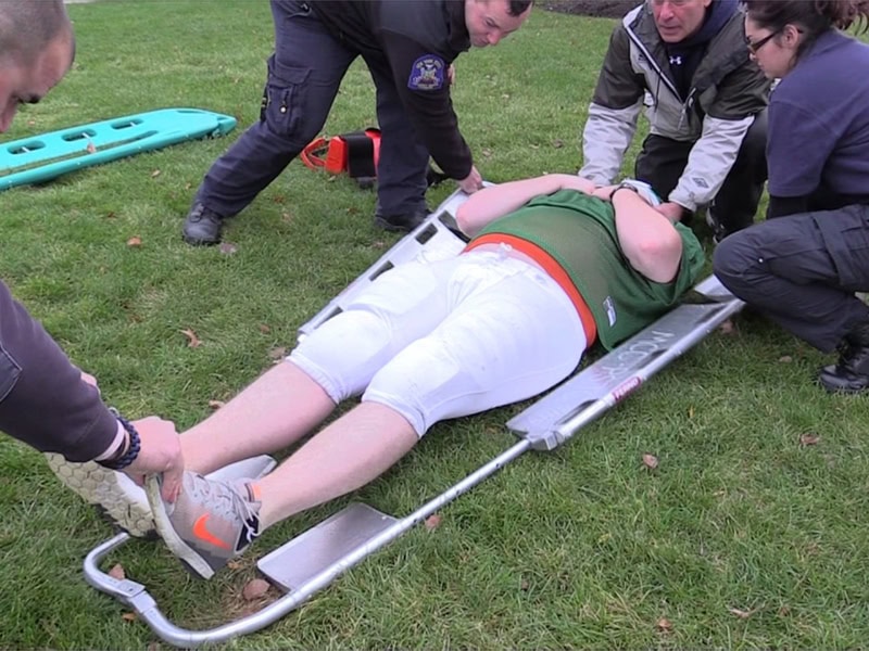 Rescue team assists an injured individual onto a scoop stretcher during a field emergency response.