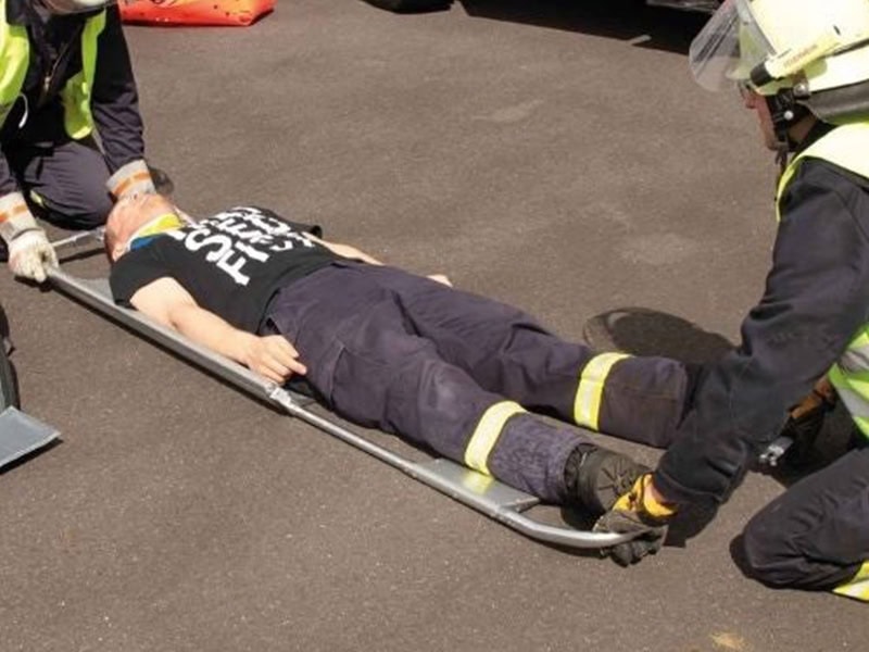 Firefighters assist an injured person secured on a scoop stretcher during a roadside emergency drill.