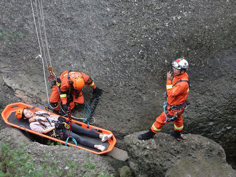 Mountain rescue team secures an injured hiker in a basket stretcher during a cliffside emergency evacuation.