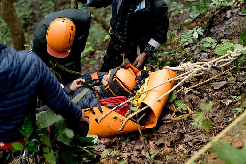Rescue team using basket stretcher to evacuate injured person from forest slope
