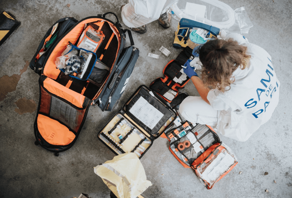 Paramedic prepares emergency medical kit on concrete floor