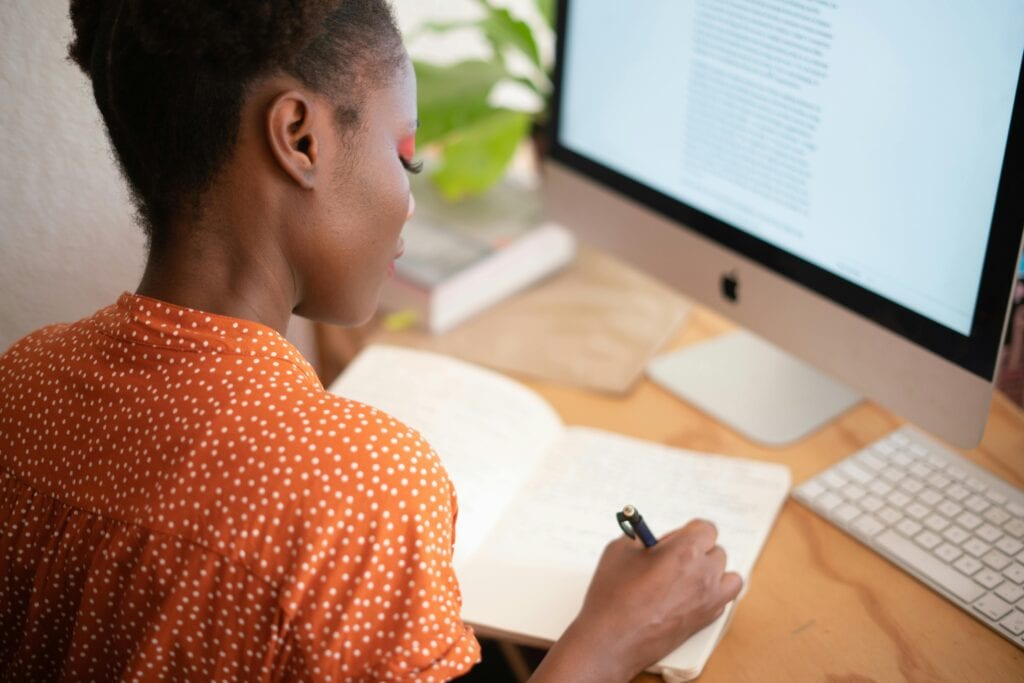 Woman taking notes at desk with computer